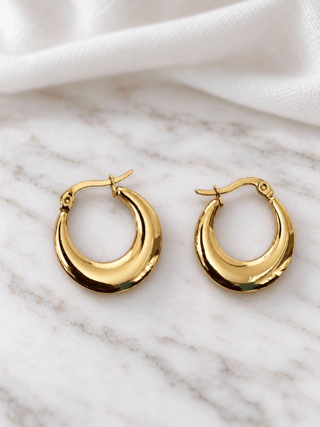 Gold crescent hoop earrings on white marble
