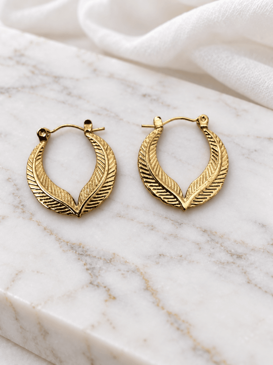 Gold feather hoop earrings on white marble