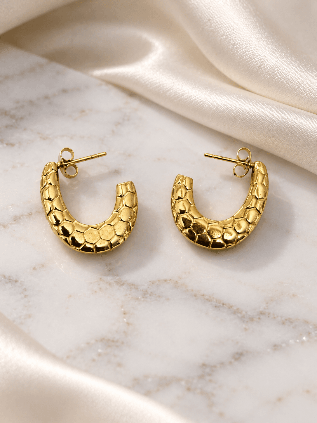 Gold pebble-textured hoop earrings on marble and ivory silk