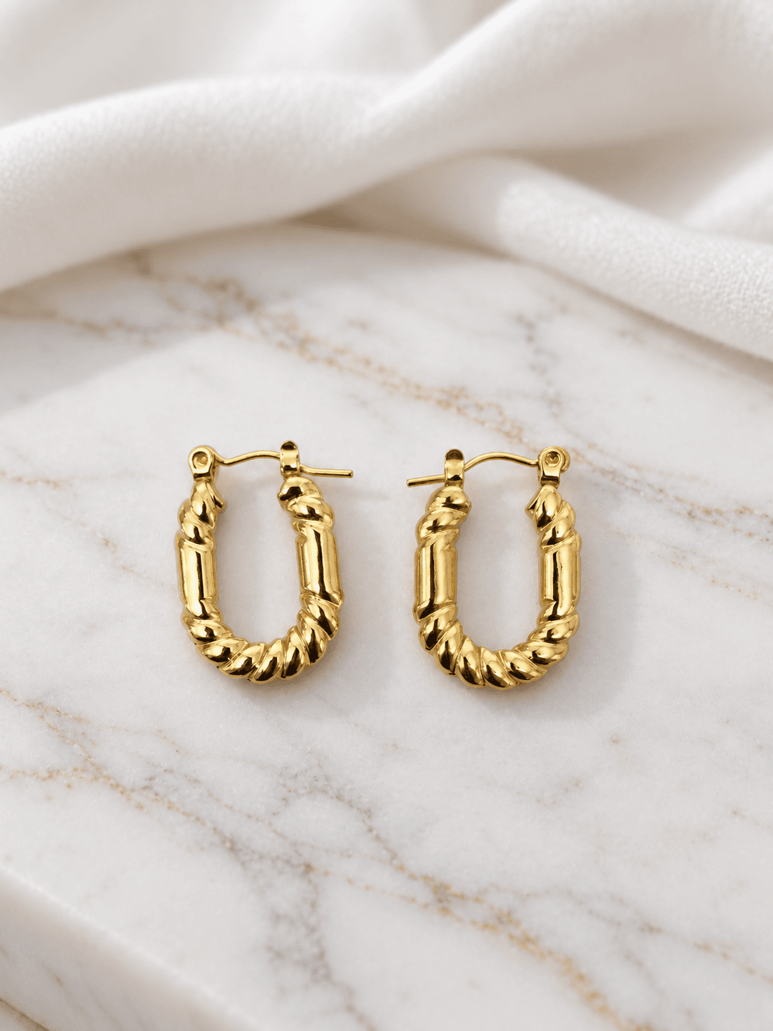 Gold ridged oval hoop earrings on white marble
