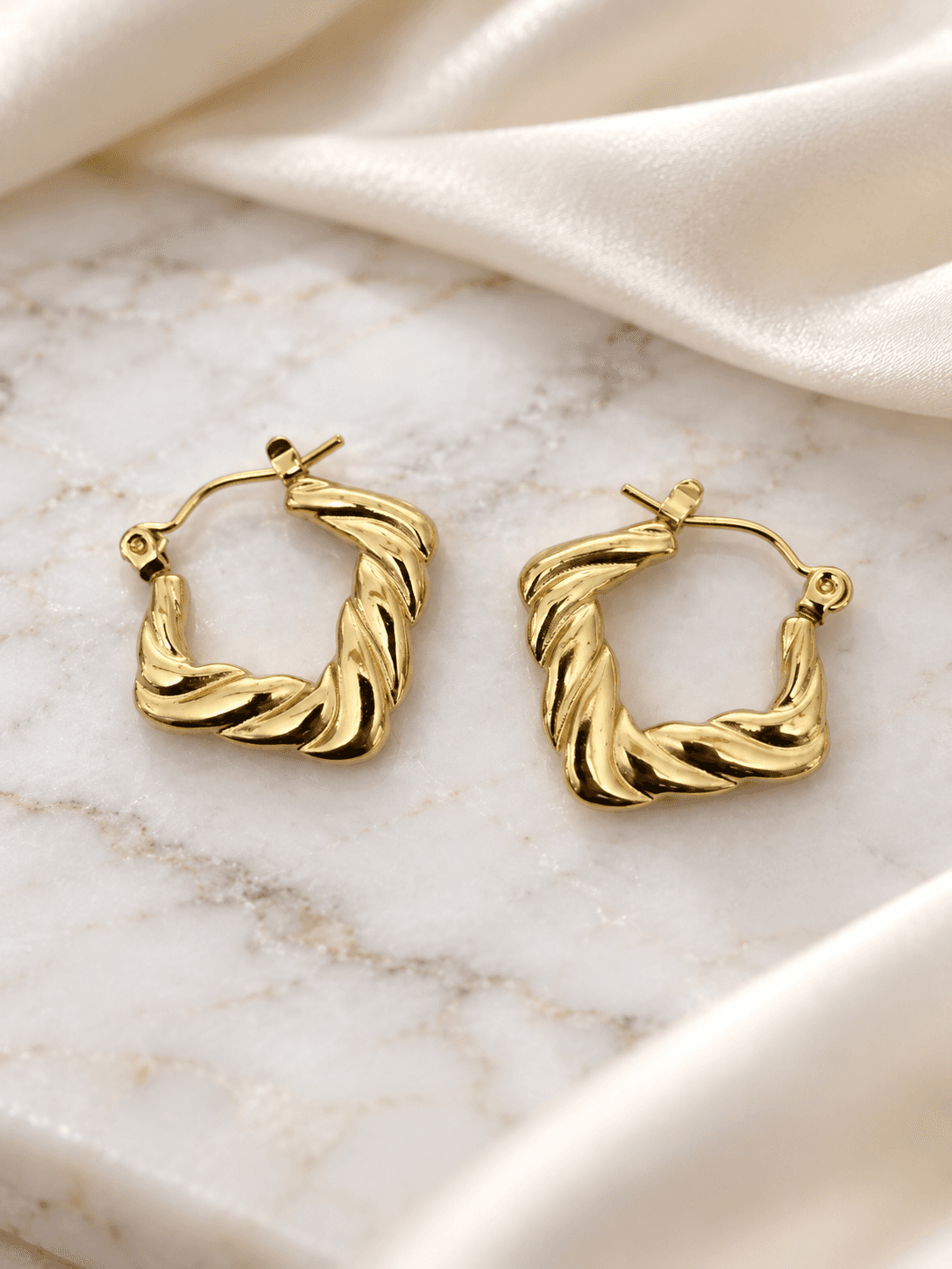 Gold square twisted hoop earrings on marble and silk