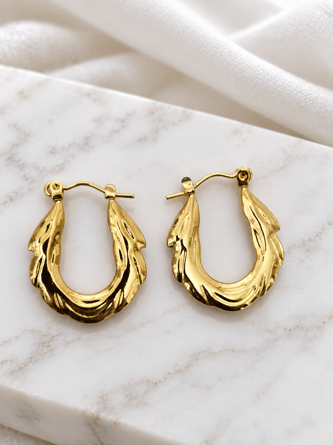 Gold twisted multi-strand hoop earrings on white marble